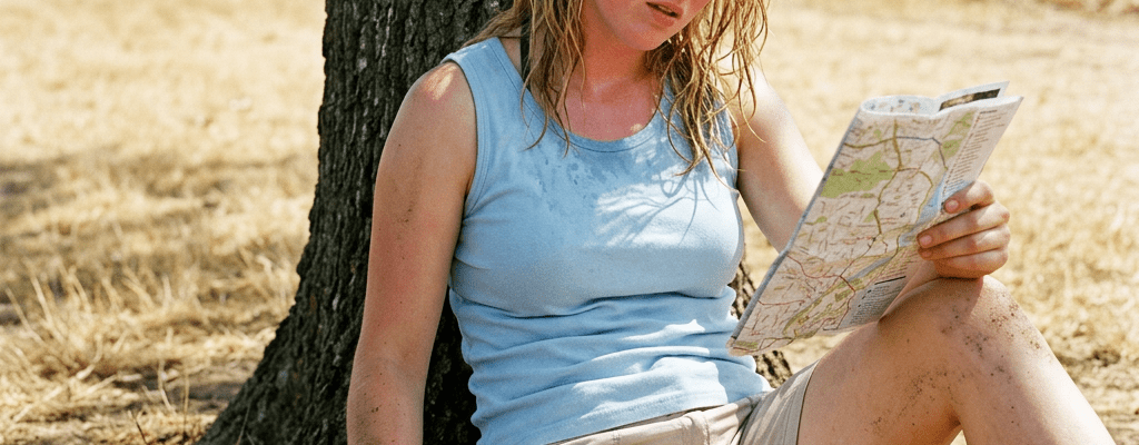 Woman sitting on ground leaning against tree, holding a map and a yellow water bottle